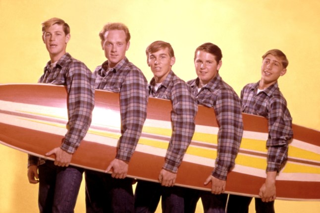 LOS ANGELES - AUGUST 1962: Rock and roll band "The Beach Boys" pose for a portrait with a surfboard in August 1962 in Los Angeles, California. (L-R) Brian Wilson, Mike Love, Dennis Wilson, Carl Wilson, David Marks. (Photo by Michael Ochs Archives/Getty Images)