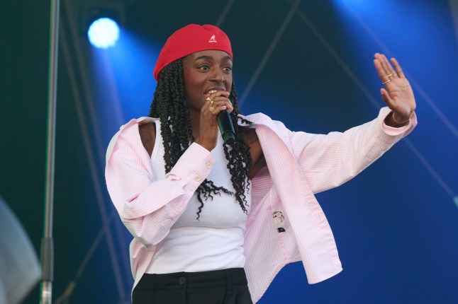 Cat Burns performs on the main stage at The Big Feastival 2024 wearibng hat and cardigan.